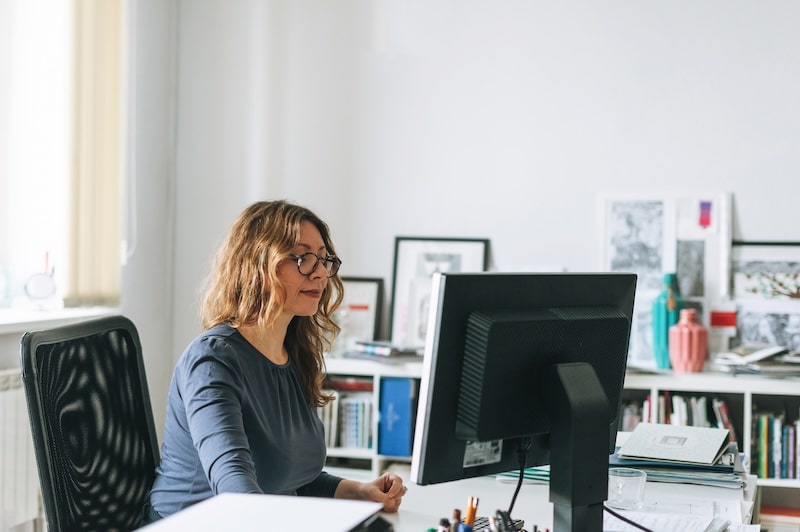 Charming smiling adult woman middle aged woman with curly hair architect designer working on computer in the bright modern office